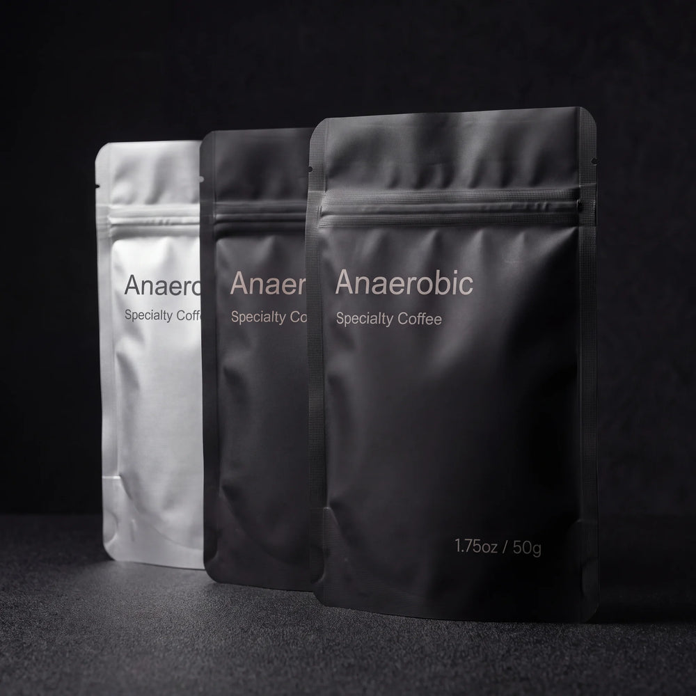 Three Anaerobic 50 g sample pouches, one silver and two matte black, on a dark surface