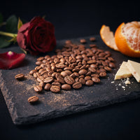 Colombia Nativo Nogales Reserve tasting-note still life — roasted beans with red rose, tangerine and white chocolate on slate