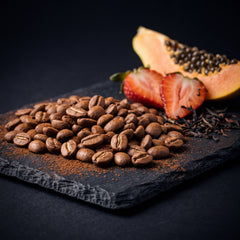 Ethiopia Dawencho Anaerobic Natural G1 tasting-note still life — roasted beans with papaya, strawberry and black tea leaves on slate