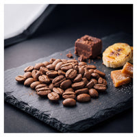 Uganda Coffee Yards 48h anaerobic natural tasting-note still life — roasted beans with chocolate fudge, caramelized banana and toffee on slate